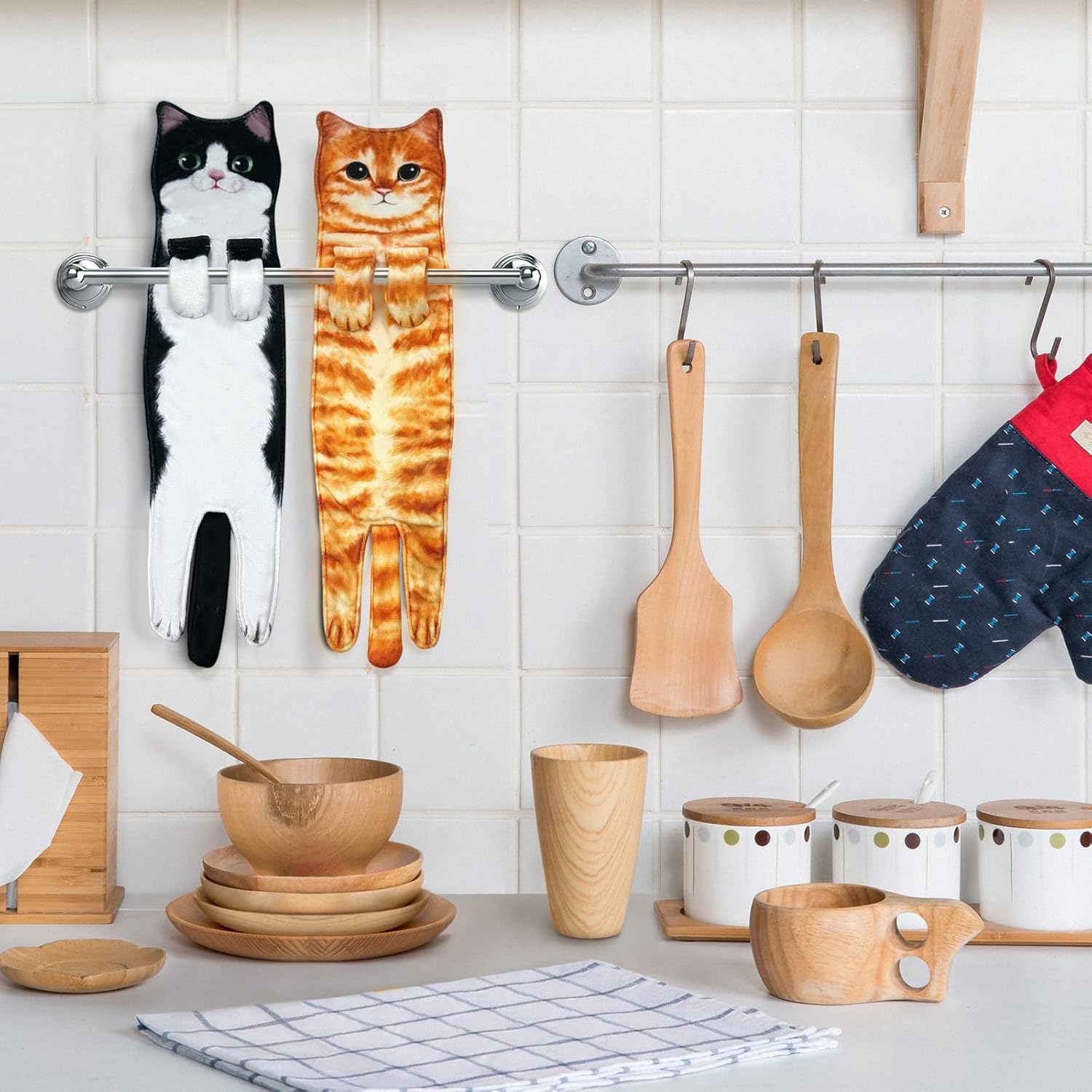Tuxedo and orange cat towels hanging on a kitchen rail beside wooden utensils